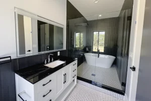 Bright bathroom with glass shower door, black and white vanity, and patterned tile flooring.