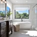 Bright bathroom featuring glass shower enclosure, mirror, and elegant bathtub with natural light.