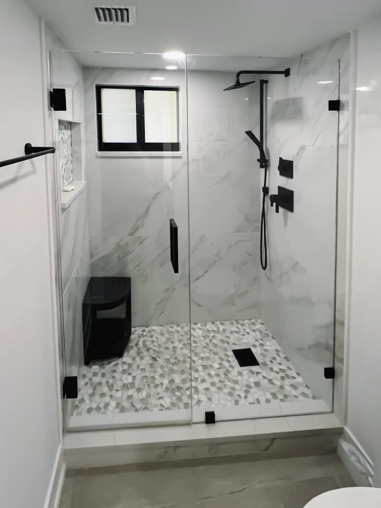Modern black-framed glass shower with marble walls, pebble floor, and sleek fixtures for luxury bathroom design.