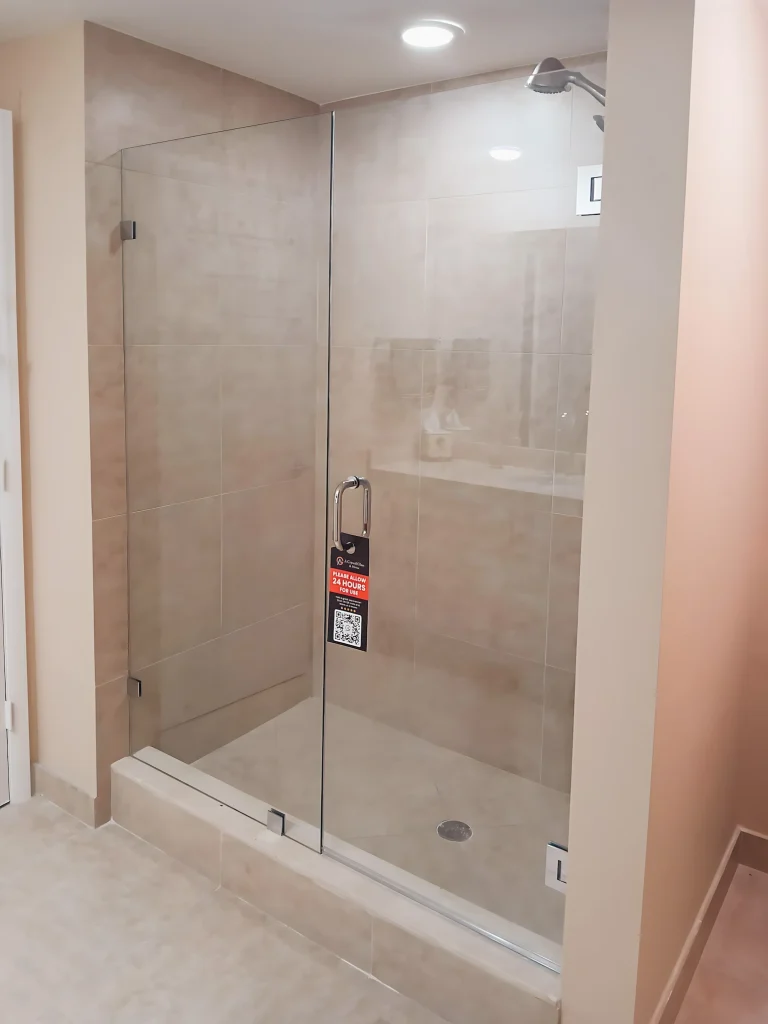 Shower glass door with sleek chrome handle and beige tiled walls.