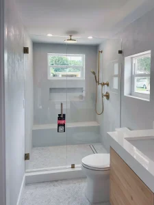 Bright bathroom with glass shower enclosure, brass fixtures, white tiles, and natural light.