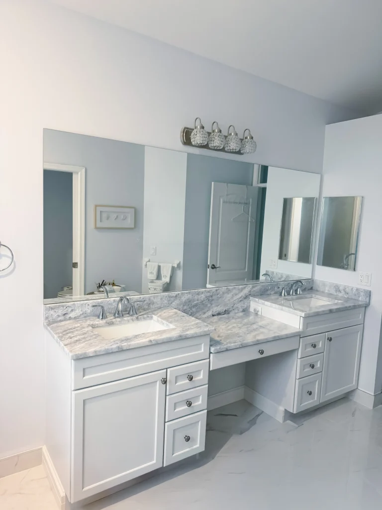 Bright bathroom featuring a white double vanity with marble countertops and mirrored cabinets.