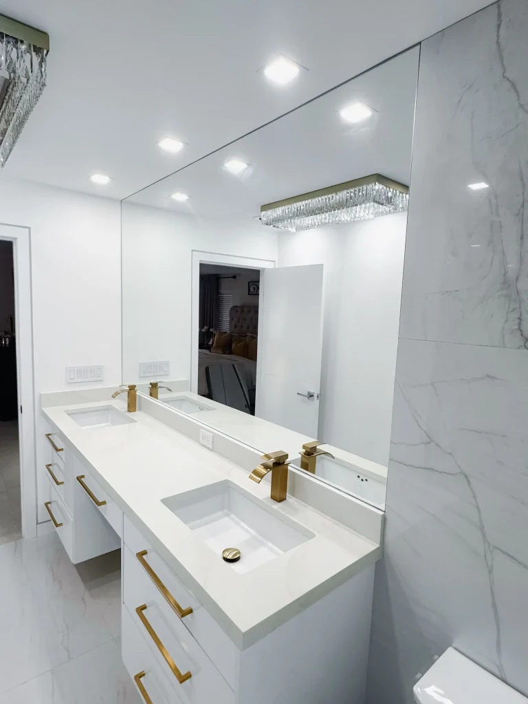 Luxury glass and mirror bathroom with sleek white surfaces and gold hardware.
