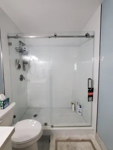 The image showcases a modern glass shower enclosure with a sliding door and brushed nickel hardware. It features built-in shower accessories and a minimalist design.