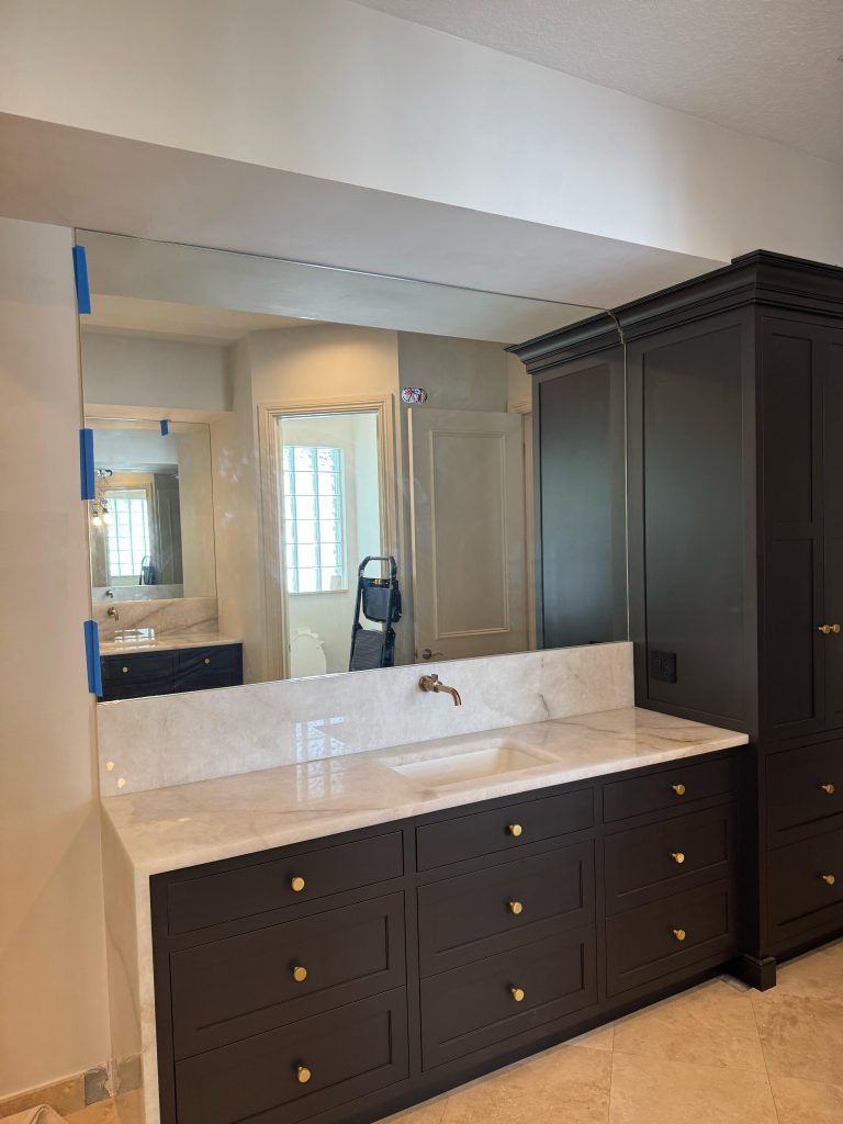 Stunning bathroom mirror and black cabinetry with gold accents in a modern bathroom design.