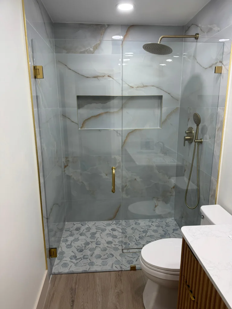 High-quality glass shower door with gold hardware, marble tile walls, and stylish pebble stone floor.