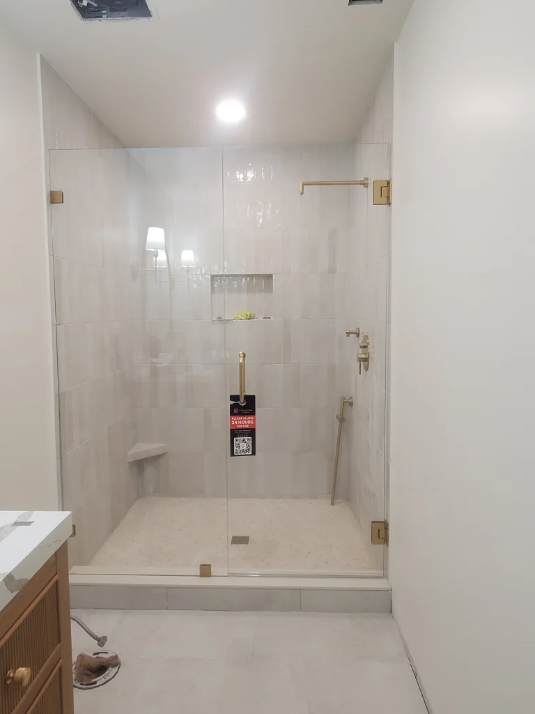 Shower glass door with gold hardware, tile walls, modern bathroom design, transparent enclosure.