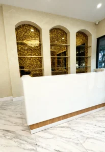 Sleek white reception desk with glass shelves and gold patterned mirrors behind.