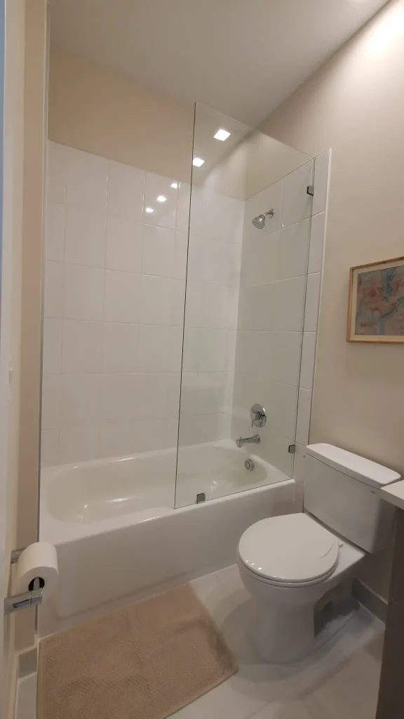 Clear glass bathroom shower partition, modern showerhead, and tub with clean tile design.