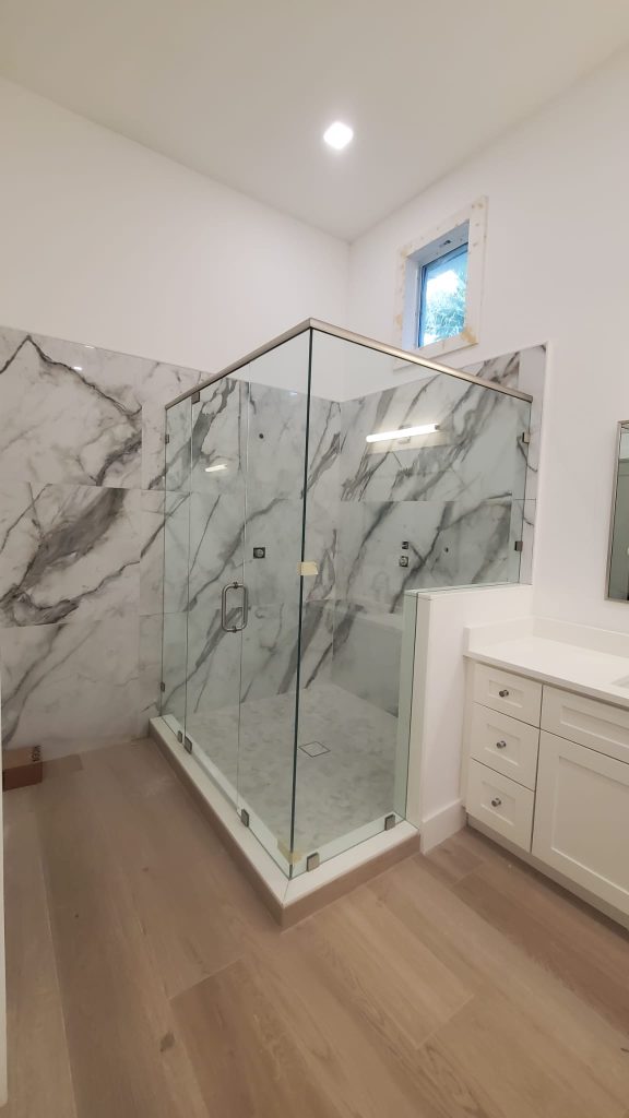 Custom glass shower enclosure featuring clear frameless glass and marble walls for luxury bathrooms.