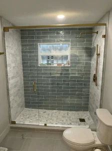 Glass shower enclosure with brass hardware and gray tile walls.