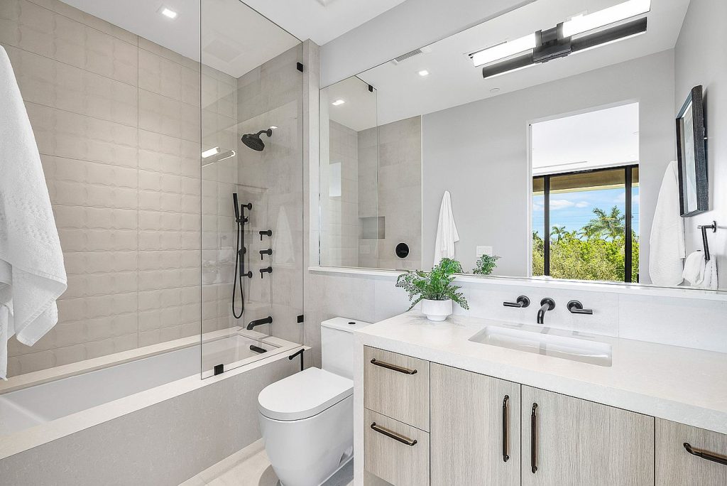 Glass shower with sleek black fixtures and large mirror in contemporary bathroom.