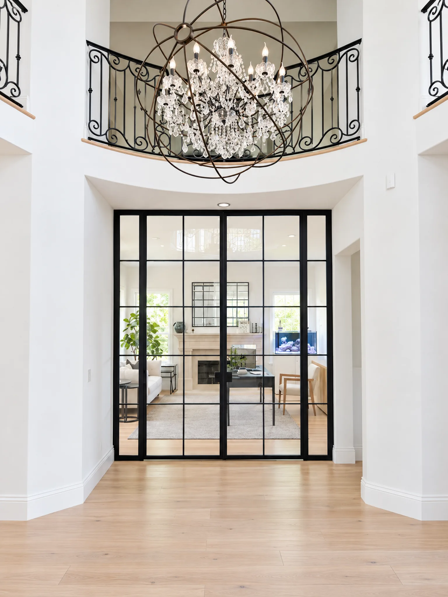 Black steel and glass doors under a chandelier in a two-story foyer