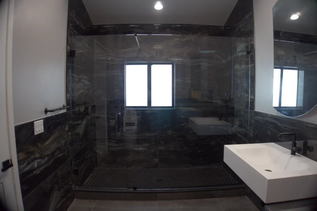 Frameless door and panel shower with matte black hardware in a dark marble guest bath, Audubon Trail Residence, Lake Worth, FL