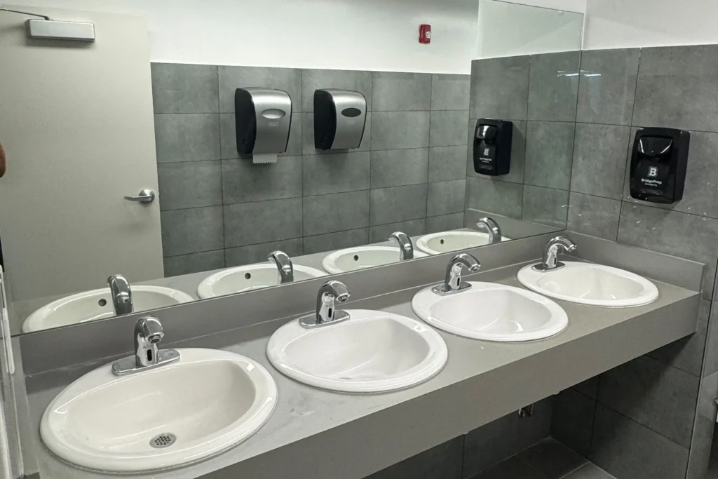 Frameless clear vanity mirrors over a multi-sink restroom counter at Bridge Prep Academy Green Village, Miami
