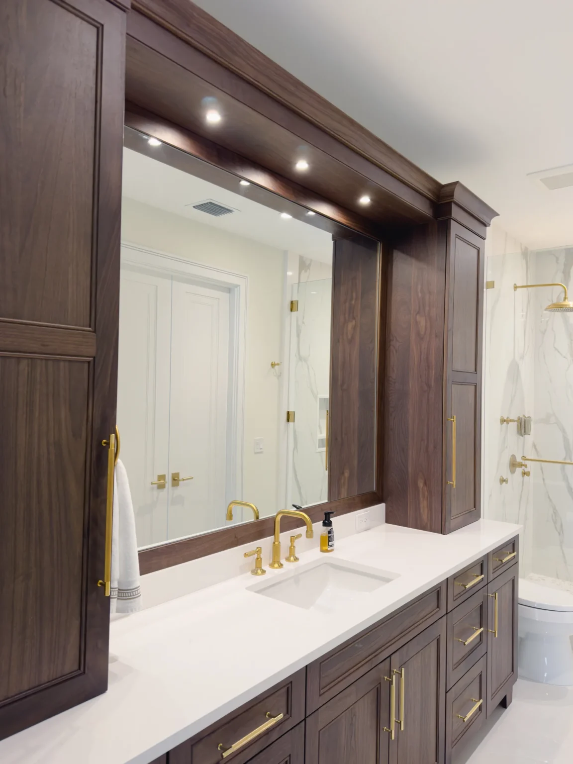 Custom vanity mirror fitted between walnut cabinets