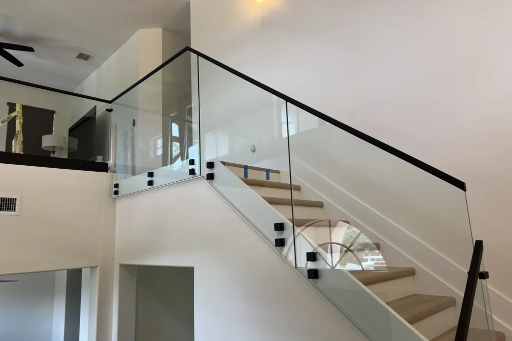 Frameless glass stair and landing railing with matte black standoffs and top rail in a Lake Worth home