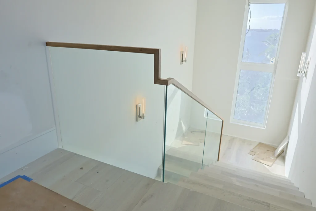 Glass stair railing with stepped wood cap rail at the upper landing of a Stuart, FL home