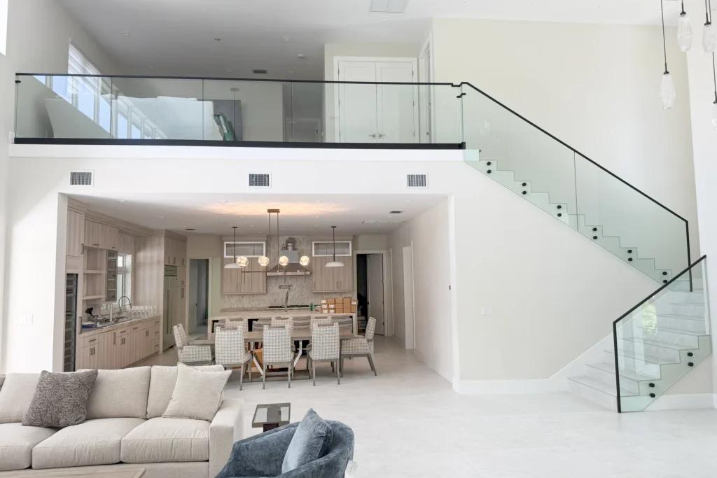 Open-plan living area with a glass staircase railing and glass loft guard with black cap rail in West Palm Beach