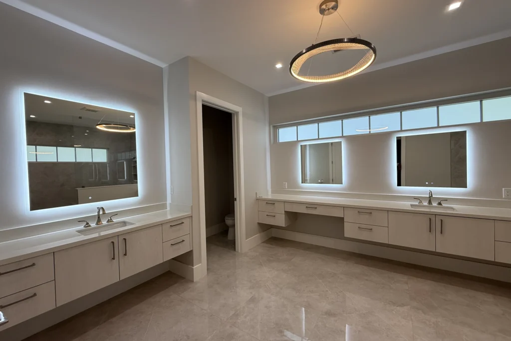 Primary bathroom with backlit LED vanity mirrors over a long double vanity in West Palm Beach