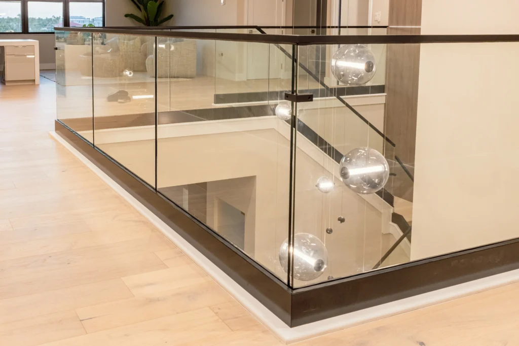 Frameless glass railing with base shoe and black cap rail around an interior stair opening, Migration Point Residence, Palm Beach Gardens, FL