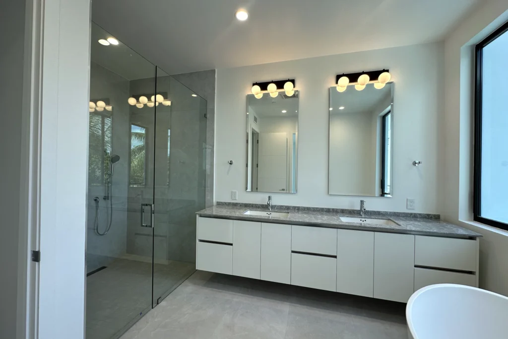 Primary bath with a frameless clear glass shower enclosure and double vanity in a Delray Beach home by ACG Glass & Metals