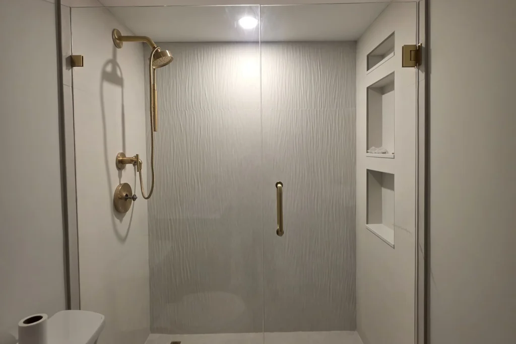 Frameless shower enclosure with satin brass hardware in a Delray Beach condo bathroom